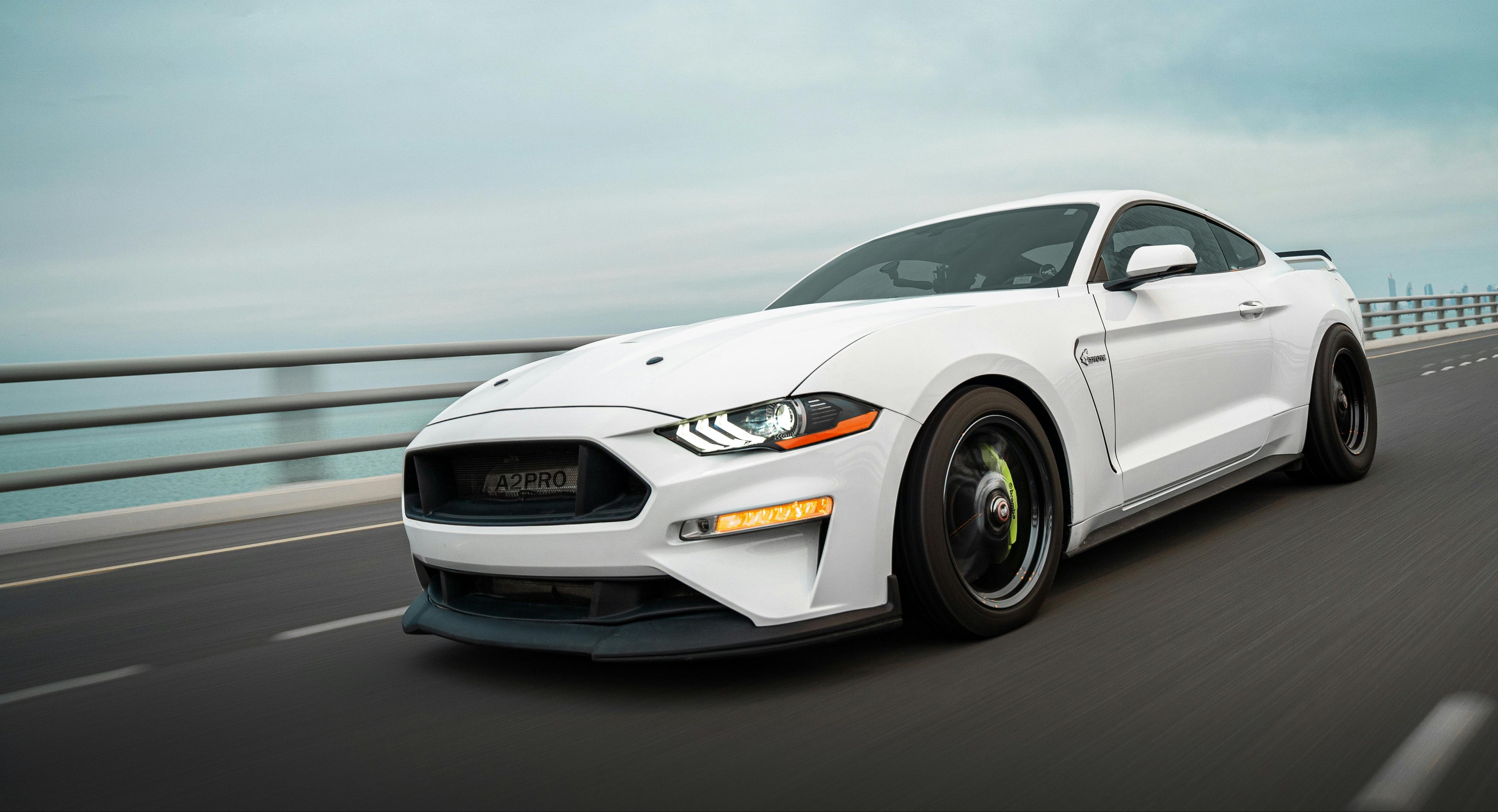 White Ford Mustang driving on a road with a cloudy sky